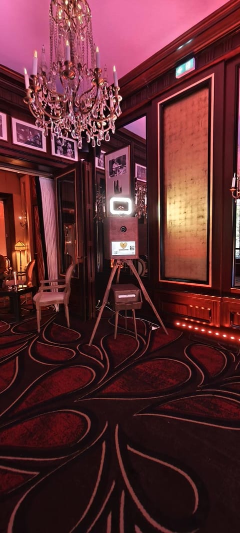 Borne photo en bois sur trépied avec son imprimante, installée sous un lustre en cristal dans un salon du Fouquet's