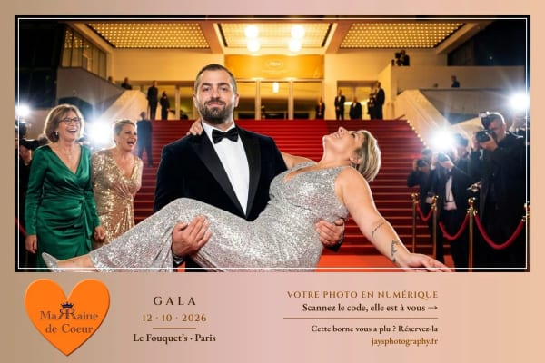 Un invité porte une invitée en robe à paillettes sur des marches au tapis rouge, photographes autour