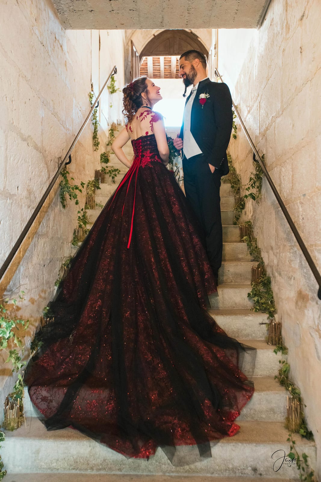Amandine et Benoit sur l'escalier de pierre médiéval, traîne bordeaux descendant sur les marches, mariage au Abbaye Royale du Moncel, par Jean-Baptiste Argyre (Jaysphotography)