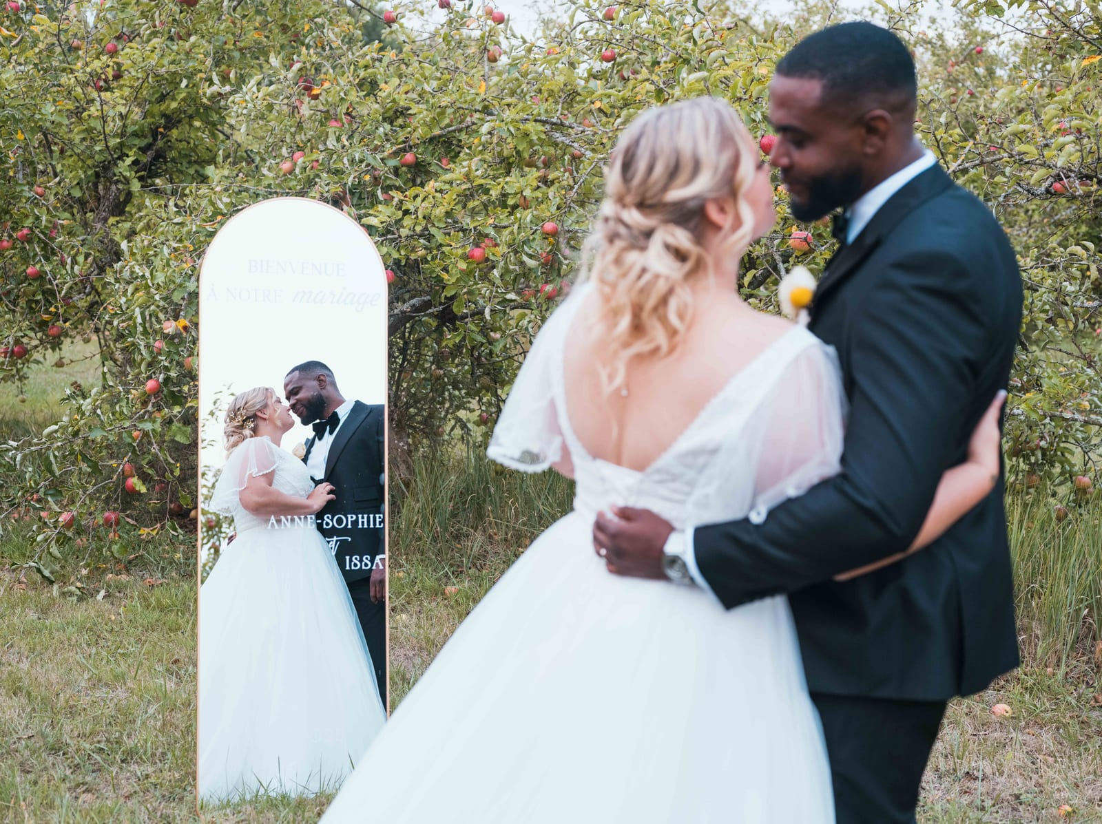 Anne-Sophie et Issa enlacés dans la végétation du domaine, robe blanche et costume sombre, lumière verte filtrée, mariage au Domaine du Mont Rouge, par Jean-Baptiste Argyre (Jaysphotography)