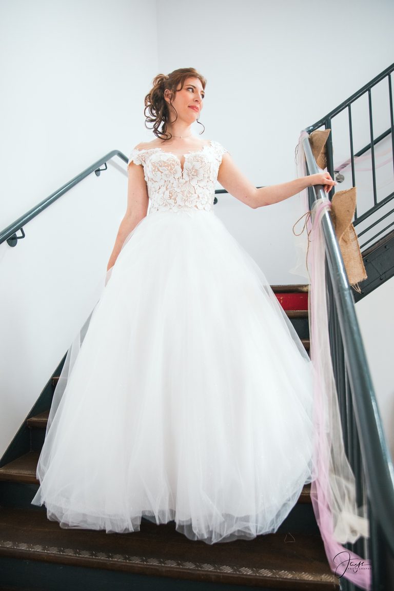 Auréline en robe de mariée princesse descend l'escalier, main sur la rampe, au Château de Broyes