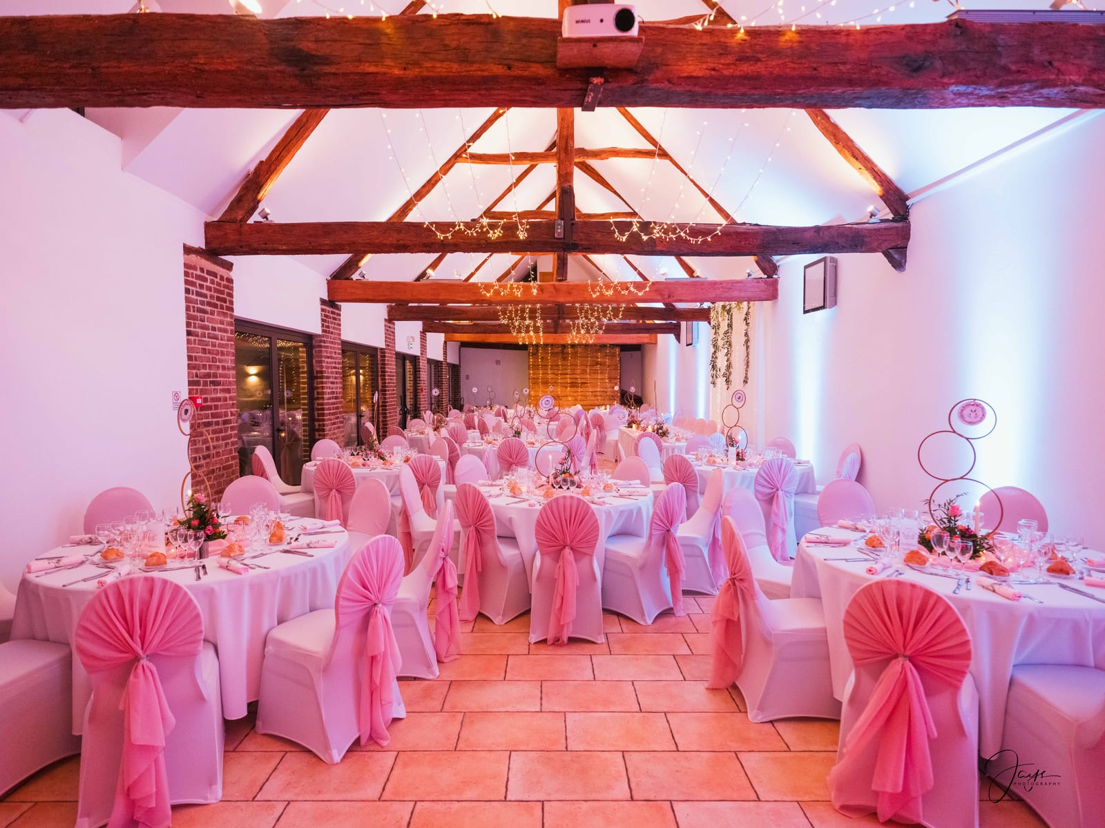 Intérieur de la salle à charpente apparente dressée pour le repas, décoration rose et blanche, mariage Christelle et Milton, photo Jaysphotography., mariage au Domaine de la Croix Sauvalle, par Jean-Baptiste Argyre (Jaysphotography)