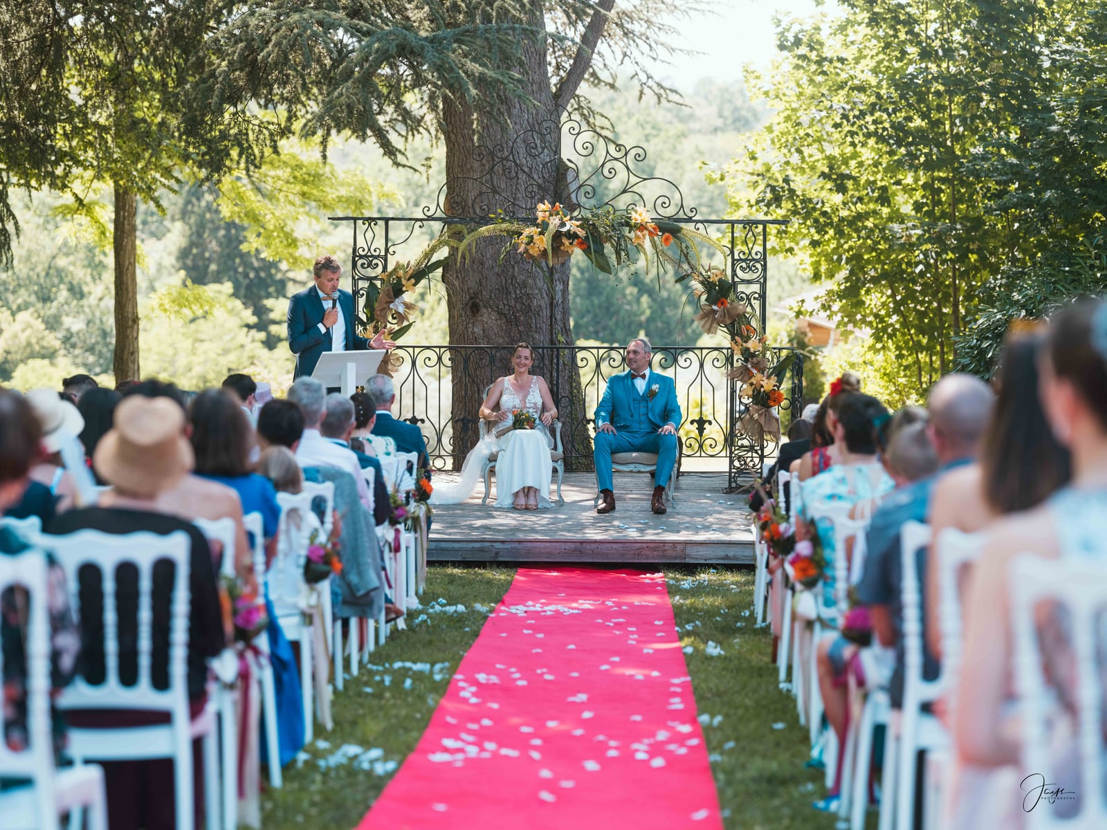 Cérémonie laïque en plein air, chaises blanches sur la pelouse et fond d'arbres du domaine, mariage au Domaine de la Fauconnie, par Jean-Baptiste Argyre (Jaysphotography)