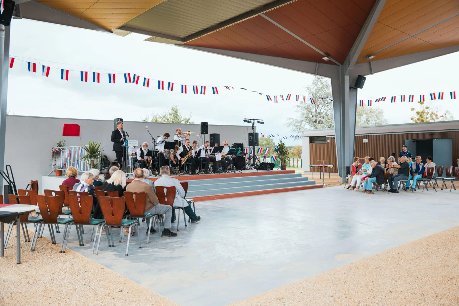 La halle couverte de Breuil-le-Vert le jour de son inauguration, l'orchestre Jazz & Co. sur la scène et le public installé sous la charpente, guirlandes tricolores, mariage au Breuil-le-Vert (Oise), par Jean-Baptiste Argyre (Jaysphotography)