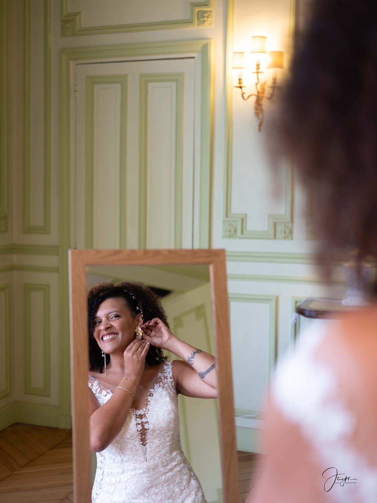 Jennifer face au miroir, ajuste ses bijoux, robe dentelle aux reflets chauds, mariage au Château de Pontarmé, par Jean-Baptiste Argyre (Jaysphotography)