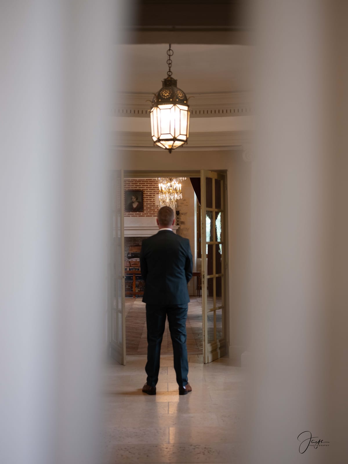 Eddy de dos dans le couloir du château, attendant le first look sous la lanterne en laiton, mariage au Château de Pontarmé, par Jean-Baptiste Argyre (Jaysphotography)