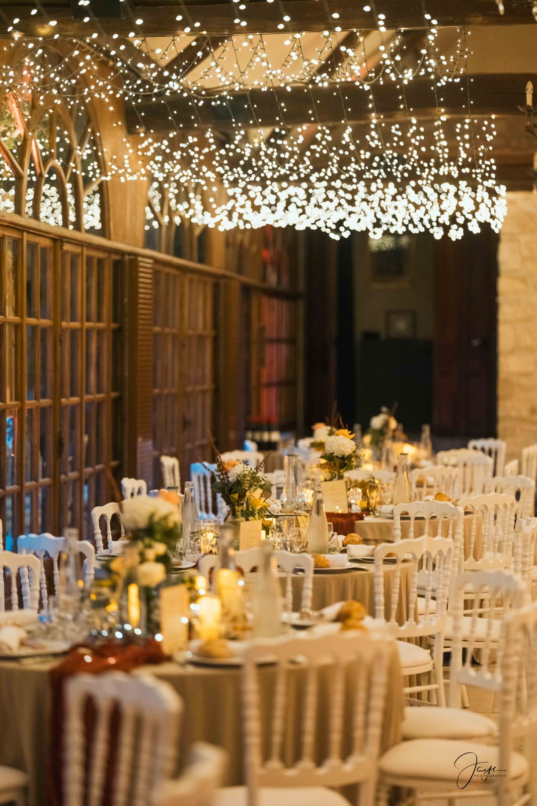 Salle de réception avec guirlandes lumineuses suspendues en voute, tables dressées en blanc, mariage au Château de Pontarmé, par Jean-Baptiste Argyre (Jaysphotography)