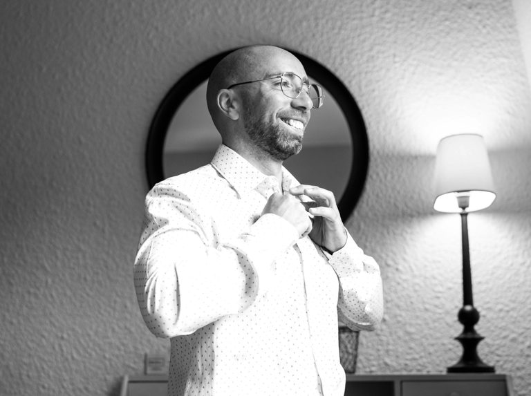 Portrait en noir et blanc de Jonathan souriant en boutonnant sa chemise devant le miroir, préparatifs au Novotel Maffliers