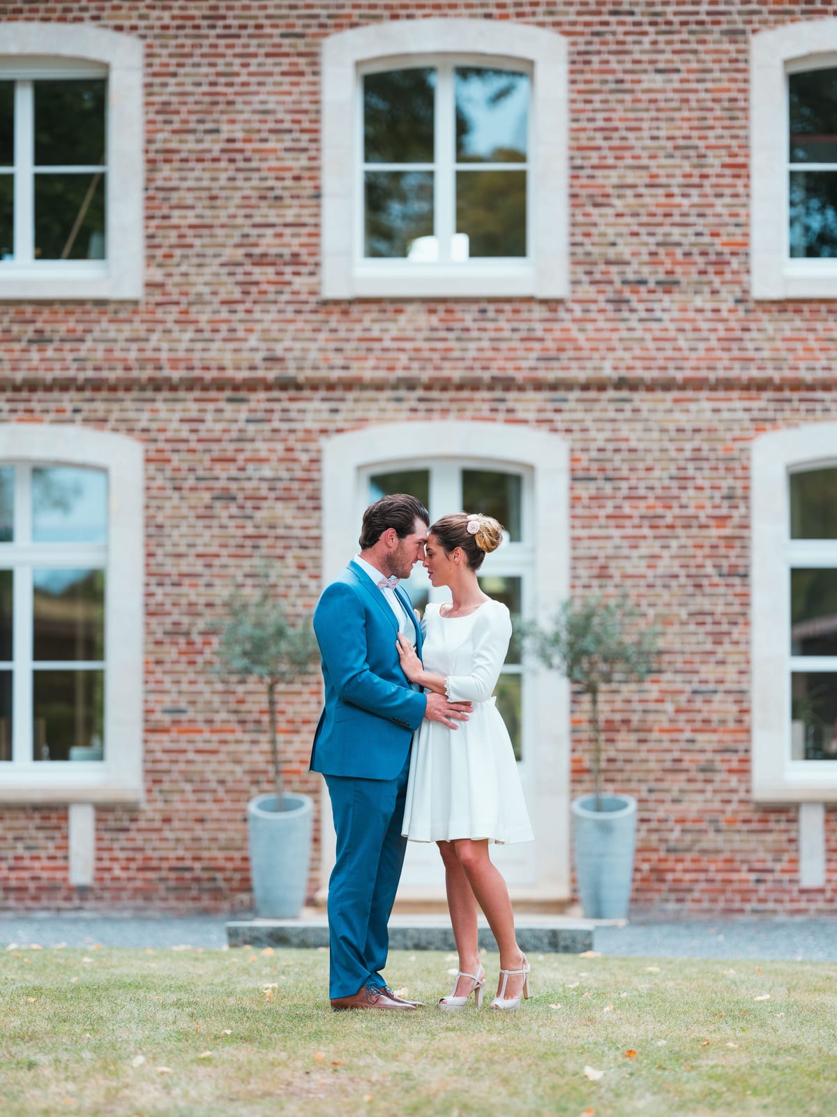 Joséphine et Armand devant la façade en brique du Château de Flixecourt, mariée en robe courte blanche, marié en costume bleu roi, mariage au Château de Flixecourt, par Jean-Baptiste Argyre (Jaysphotography)