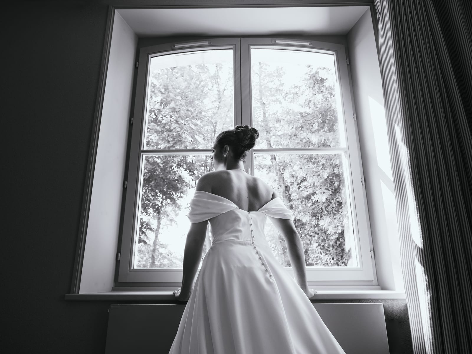Joséphine en robe longue blanche devant une grande fenêtre intérieure, lumière naturelle latérale, mariage au Château de Flixecourt, par Jean-Baptiste Argyre (Jaysphotography)