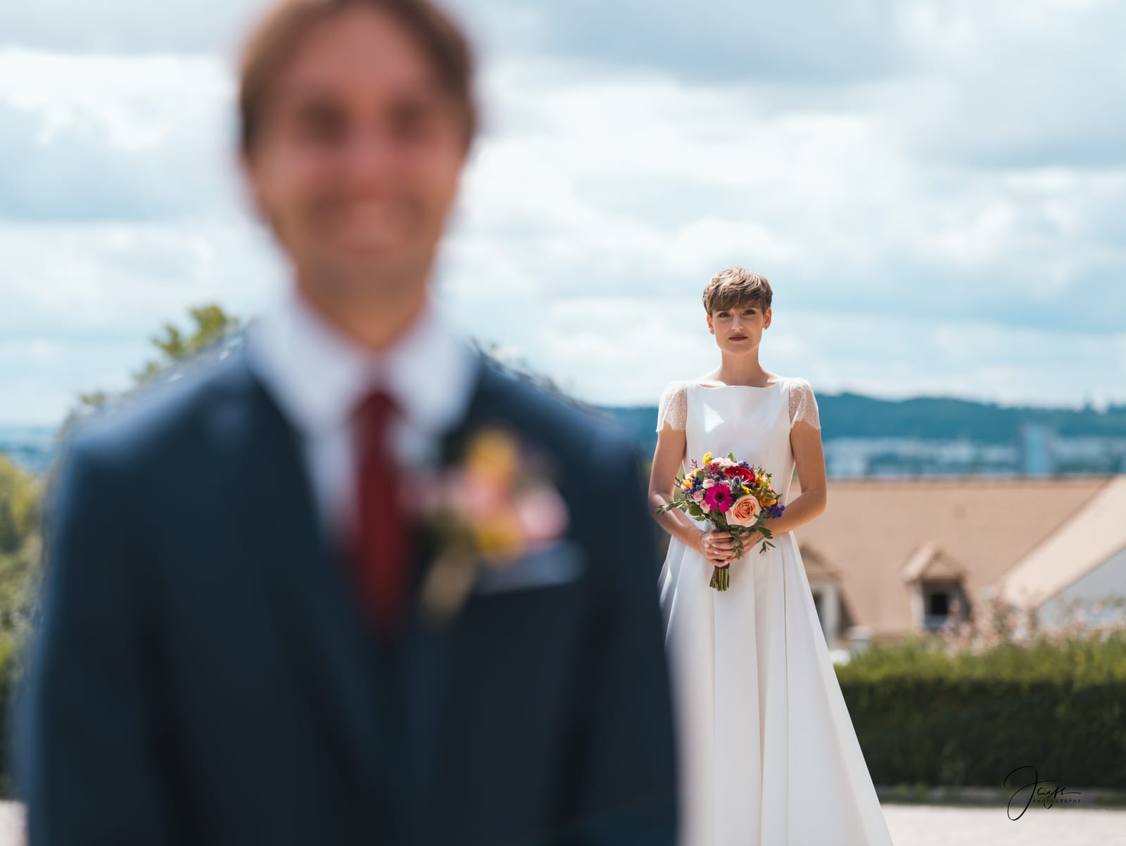 Quentin en costume bleu dans les jardins du Château de la Houssoye, ciel d'août nuageux, Lara en avant-plan, mariage au Château de la Houssoye, par Jean-Baptiste Argyre (Jaysphotography)