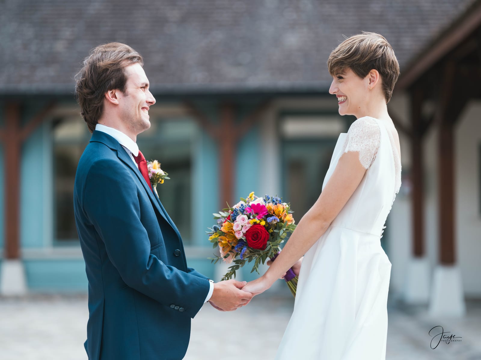 Lara et Quentin côte à côte devant la façade du Château de la Houssoye, robe blanche, costume bleu et bouquet coloré, Oise, mariage au Château de la Houssoye, par Jean-Baptiste Argyre (Jaysphotography)