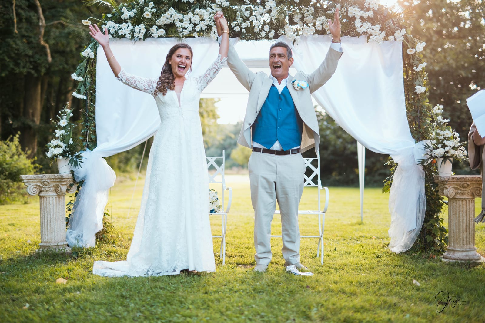 Richard tient Laura par derrière dans le parc, elle rit la tête légèrement renversée, mariage au Château de la Houssoye, par Jean-Baptiste Argyre (Jaysphotography)