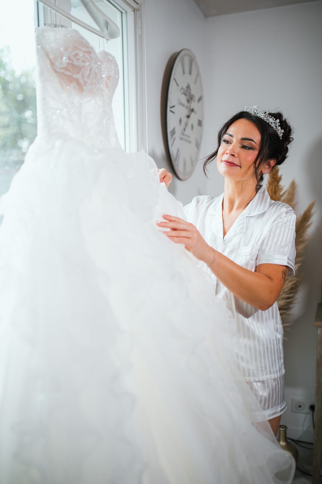 Laura en pyjama satiné ajustant sa robe de mariée près de la fenêtre, préparatifs au Domaine de la Croix Sauvalle, mariage au Domaine de la Croix Sauvalle, par Jean-Baptiste Argyre (Jaysphotography)