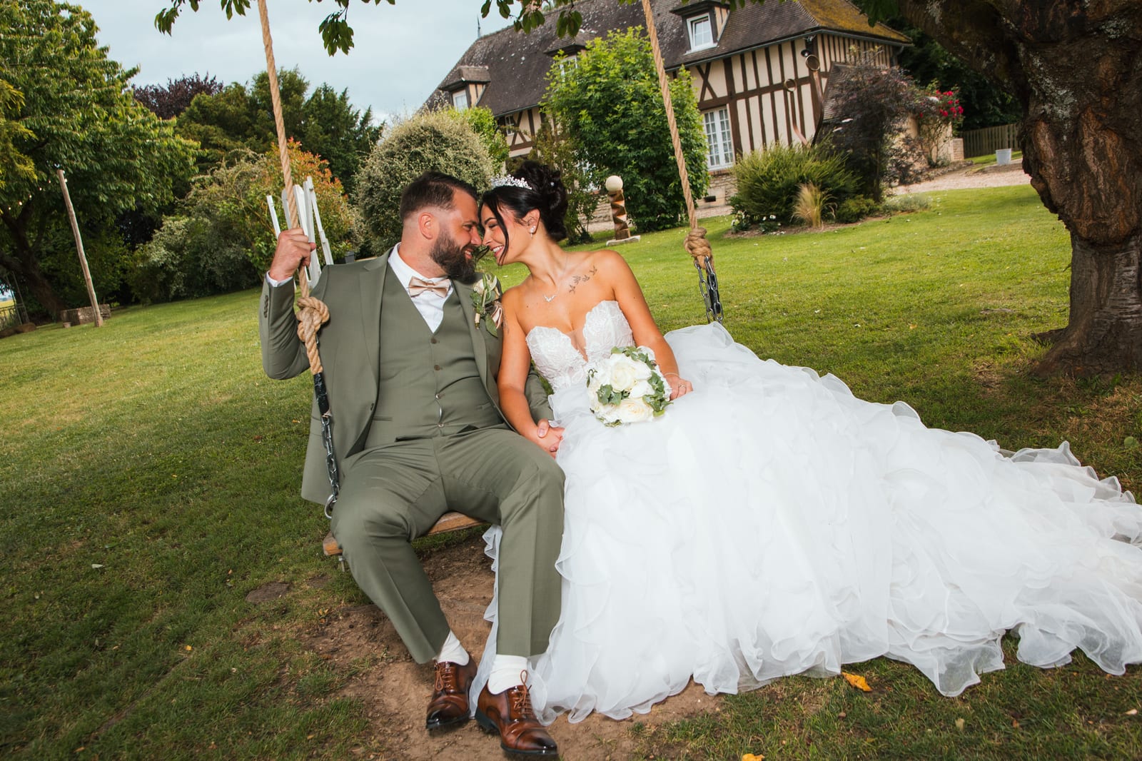 Laura et Sébastien front contre front sur une balançoire en bois face à la bâtisse normande, Domaine de la Croix Sauvalle, mariage au Domaine de la Croix Sauvalle, par Jean-Baptiste Argyre (Jaysphotography)