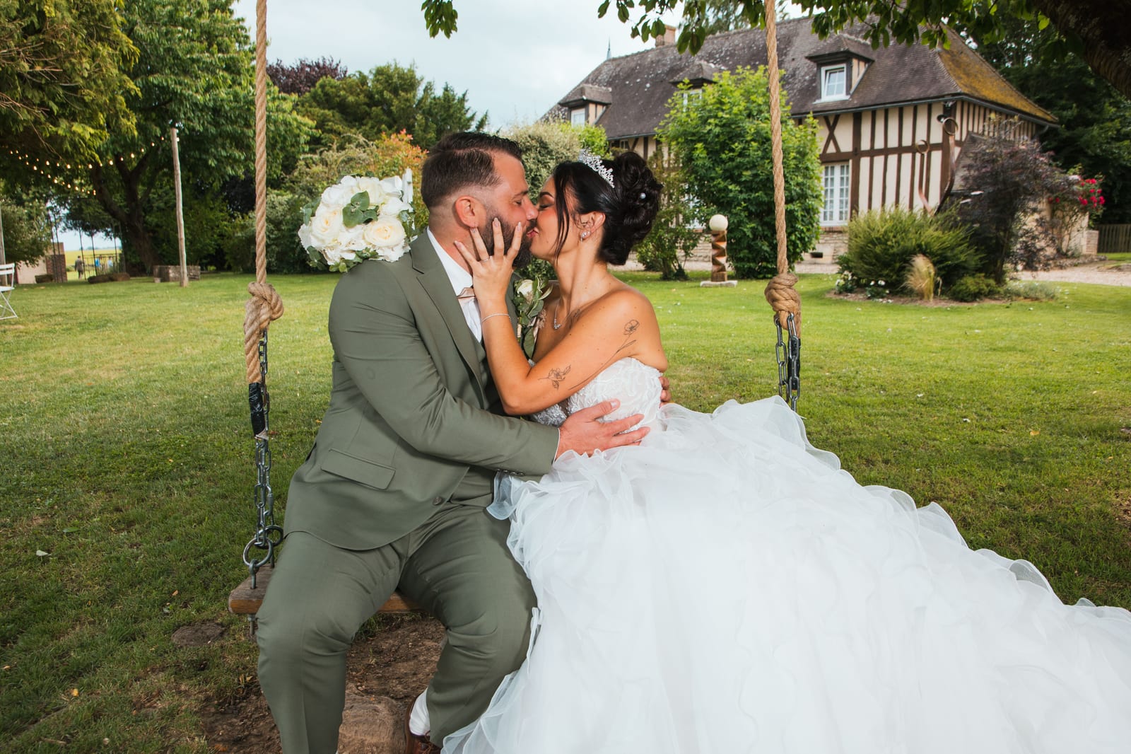 Laura et Sébastien s'embrassant sur la balançoire du parc, colombages normands en fond, Domaine de la Croix Sauvalle, mariage au Domaine de la Croix Sauvalle, par Jean-Baptiste Argyre (Jaysphotography)