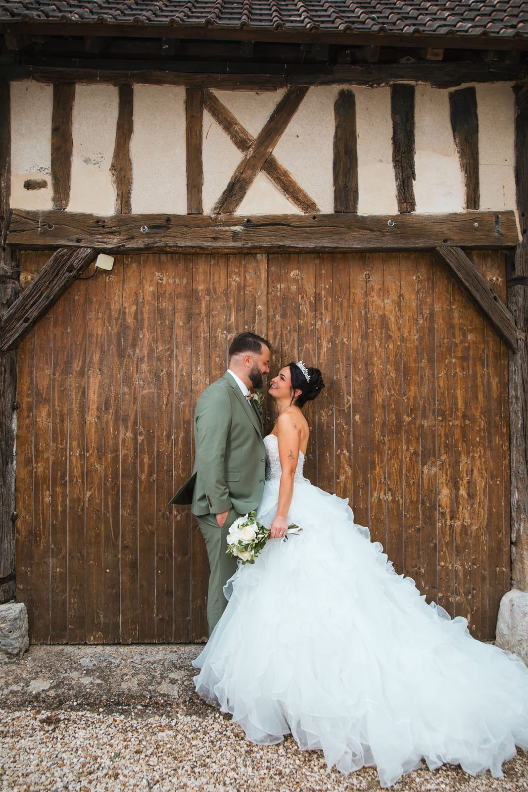 Laura et Sébastien devant la grande porte en bois de la grange à colombages, Domaine de la Croix Sauvalle, Eure, mariage au Domaine de la Croix Sauvalle, par Jean-Baptiste Argyre (Jaysphotography)