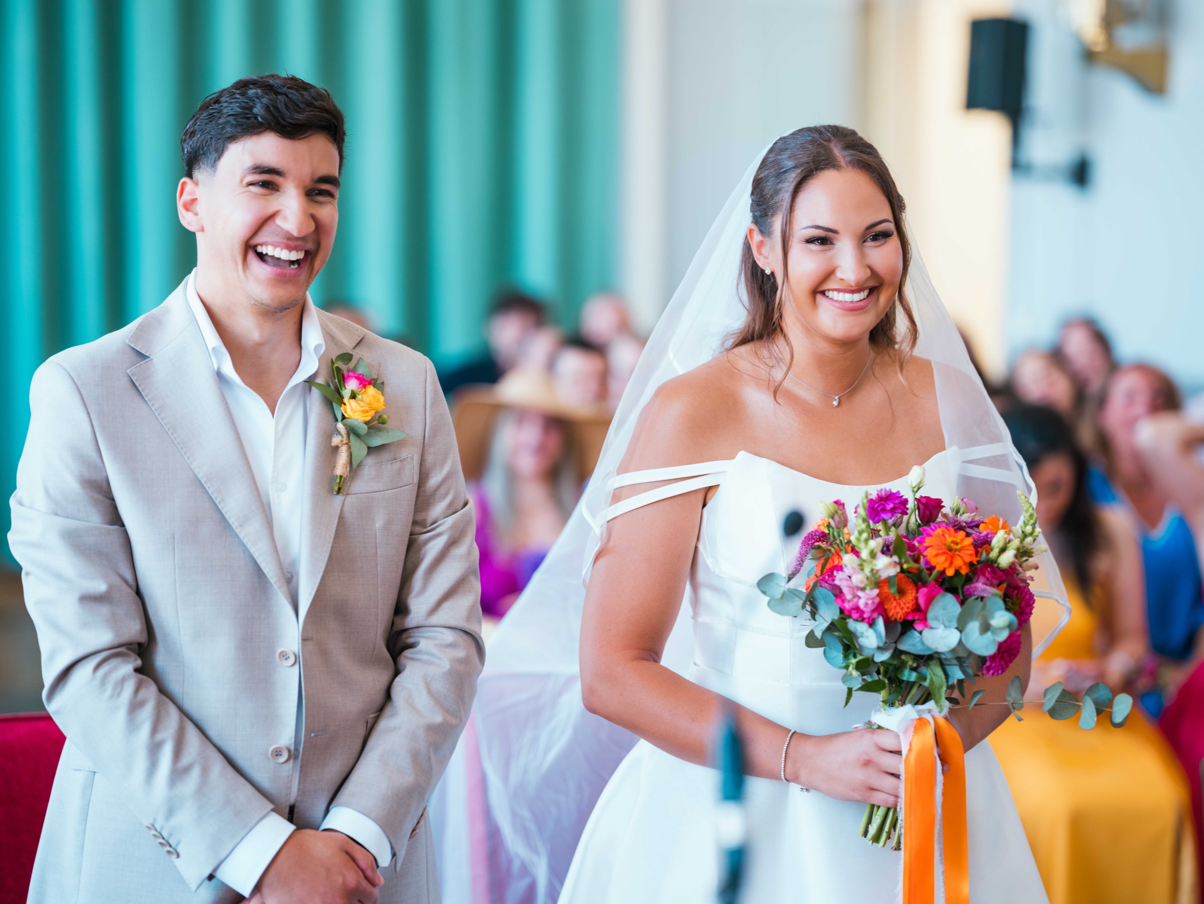 Lison et Mohammed côte à côte pendant la cérémonie, sourires francs et bouquet de gerberas orange et fuchsia, mariage au Château de Moliens, par Jean-Baptiste Argyre (Jaysphotography)