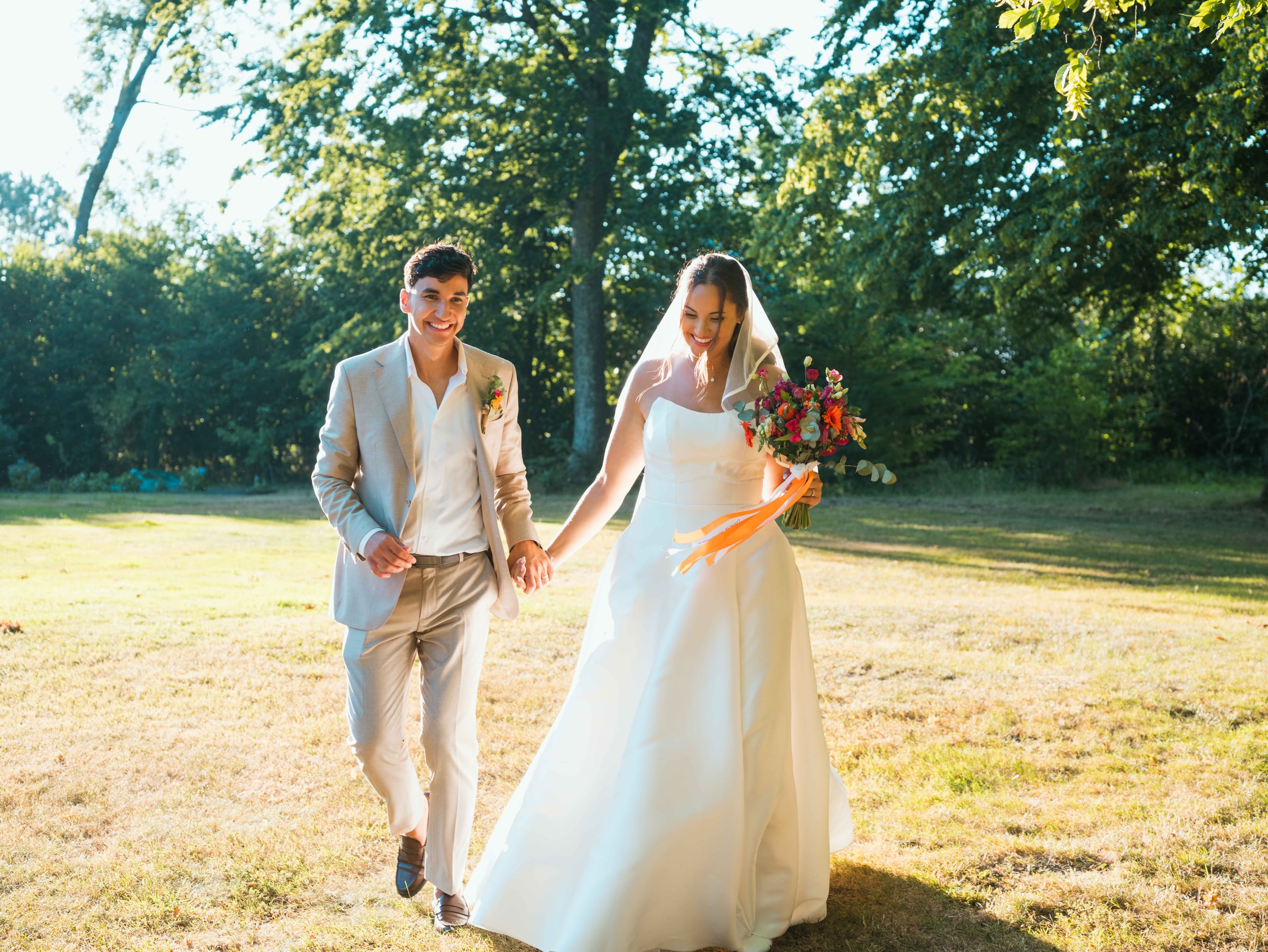 Lison et Mohammed main dans la main sur la grande pelouse du château, lumière de fin d'après-midi, mariage au Château de Moliens, par Jean-Baptiste Argyre (Jaysphotography)