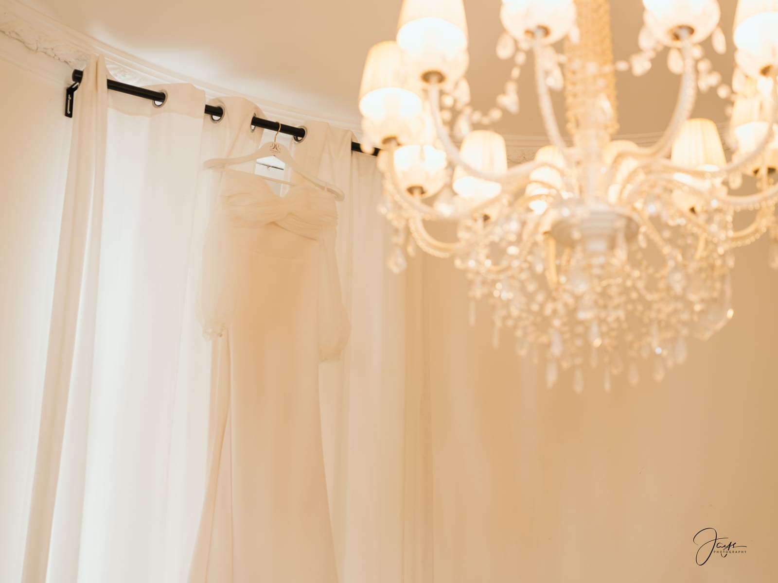 Robe de mariée suspendue sous un lustre de cristal, lumière chaude et dorée, chambre du Château d'Auvilliers, mariage au Château d'Auvilliers, par Jean-Baptiste Argyre (Jaysphotography)
