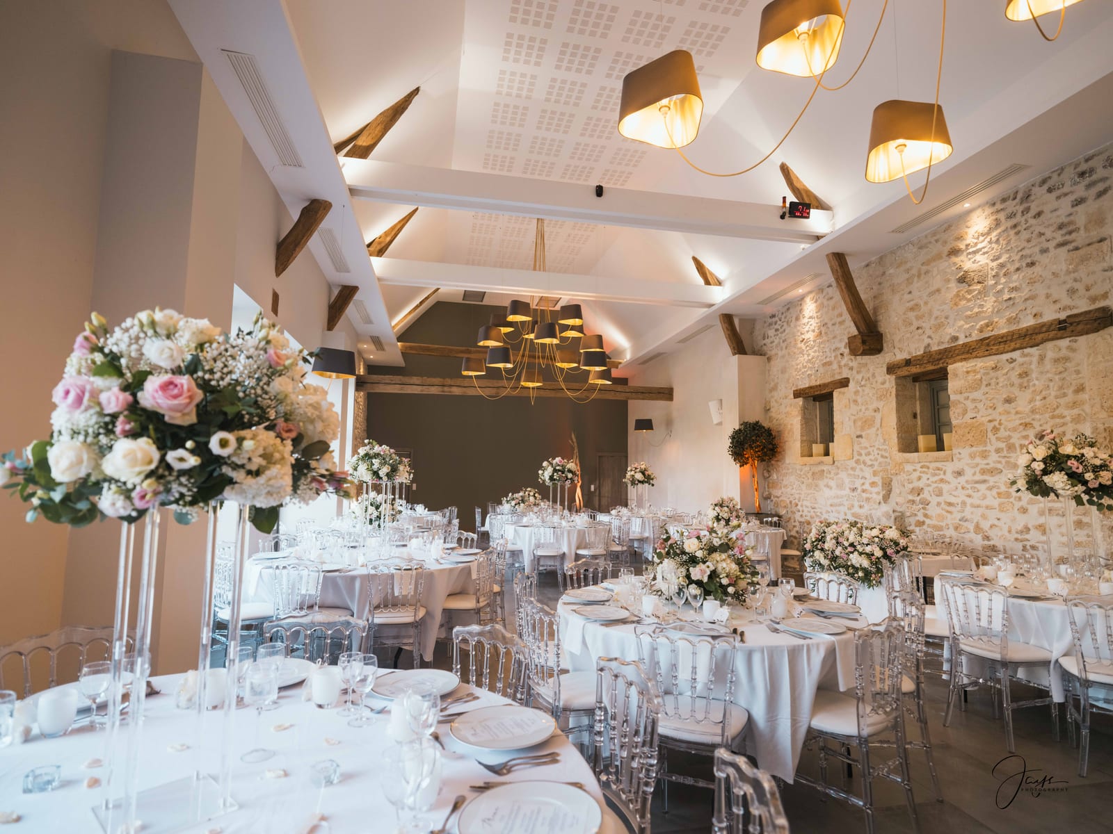 Salle de réception du Château d'Auvilliers dressée pour le diner, guirlandes au plafond, tables rondes et compositions florales hautes, mariage au Château d'Auvilliers, par Jean-Baptiste Argyre (Jaysphotography)