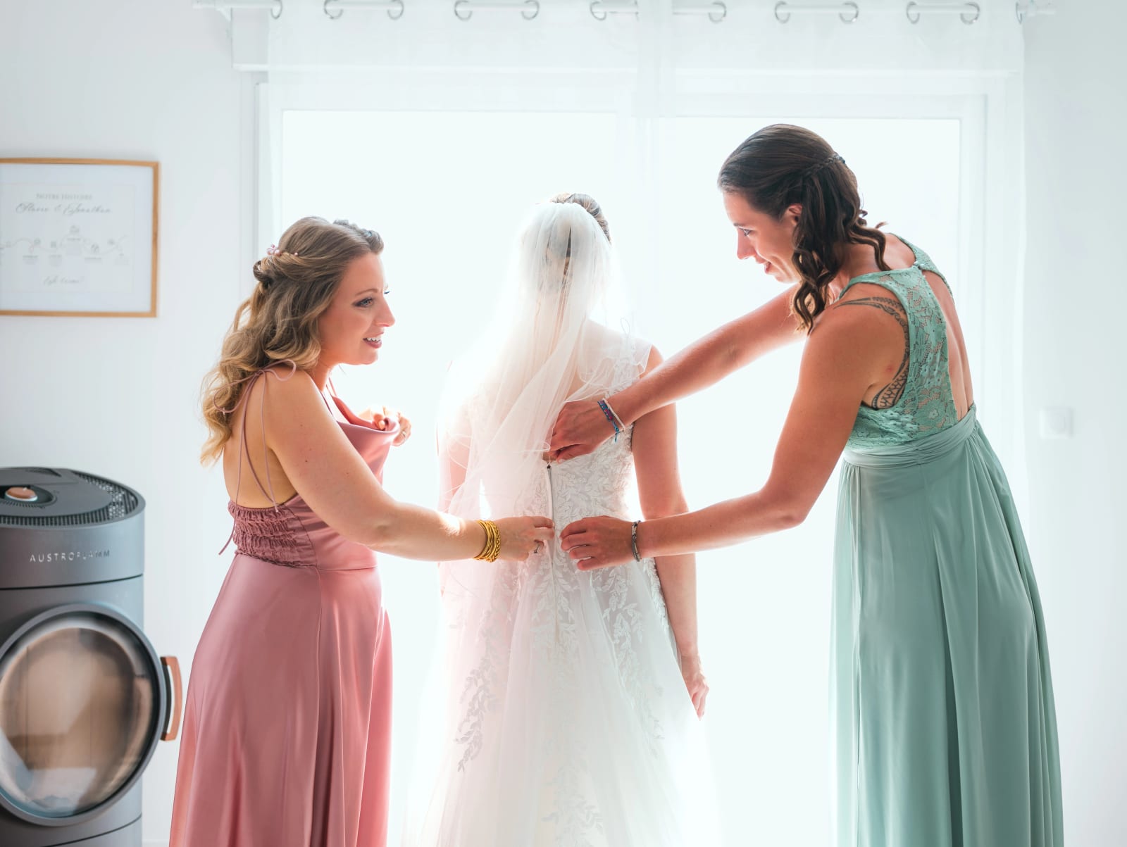 Audrey de dos en robe de dentelle et voile, deux témoins l'aident à fermer sa robe, mariage au Domaine du Bois Saint Mard, par Jean-Baptiste Argyre (Jaysphotography)