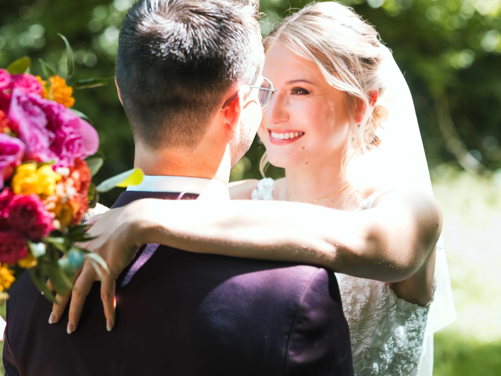 Audrey rayonnante, bras autour du cou d'Alex, son bouquet de pivoines colorées à la main, en extérieur, mariage au Domaine du Bois Saint Mard, par Jean-Baptiste Argyre (Jaysphotography)