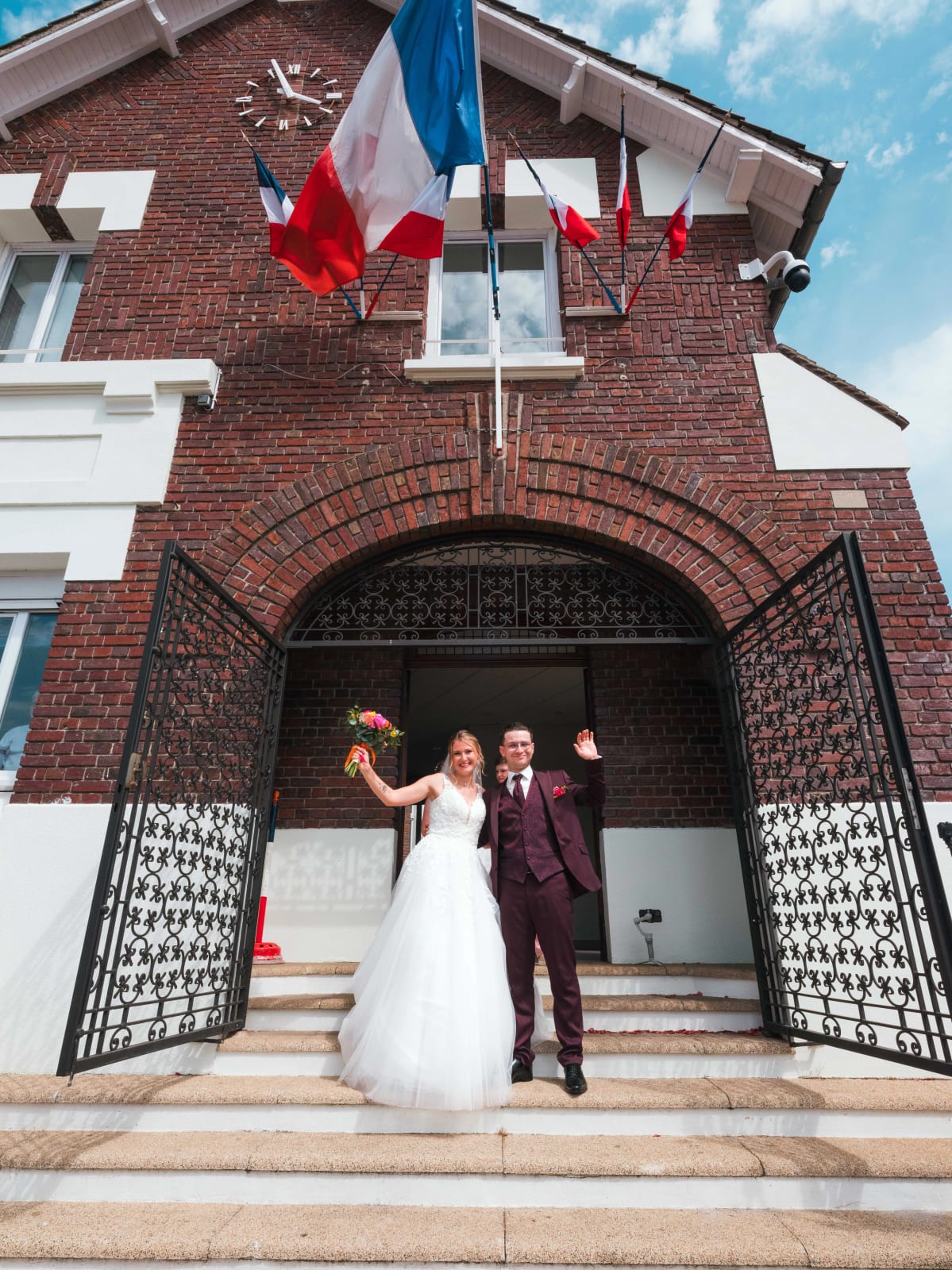 Alex et Audrey sortent de la mairie d'Estrées-Saint-Denis sous les drapeaux tricolores, bras levés, mariage au Domaine du Bois Saint Mard, par Jean-Baptiste Argyre (Jaysphotography)