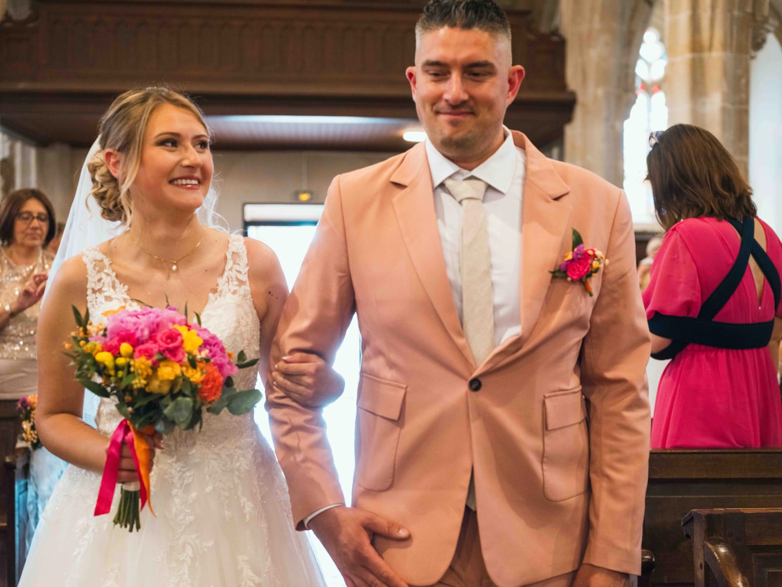 Les mariés remontent l'allée de l'église main dans la main, Alex en costume saumon, sous les applaudissements, mariage au Domaine du Bois Saint Mard, par Jean-Baptiste Argyre (Jaysphotography)