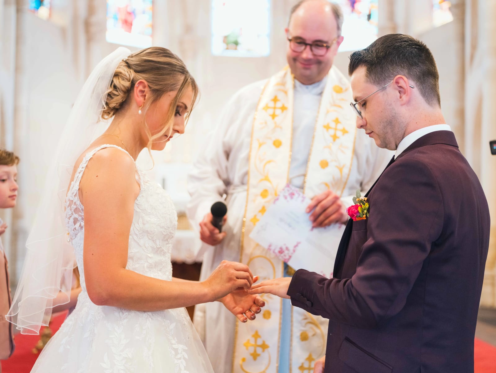 Alex et Audrey échangent les alliances face au prêtre souriant dans l'église, mariage au Domaine du Bois Saint Mard, par Jean-Baptiste Argyre (Jaysphotography)