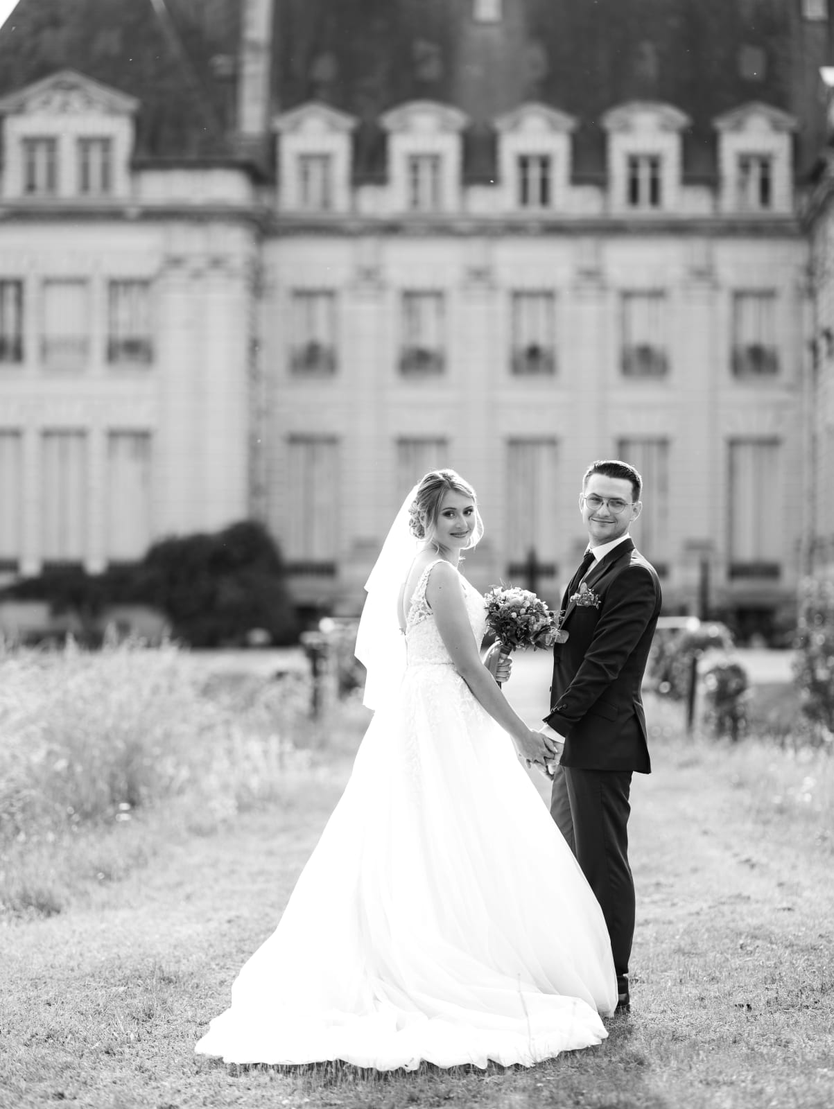 Portrait de couple en noir et blanc dans le parc du domaine, le château flou en arrière-plan, mariage au Domaine du Bois Saint Mard, par Jean-Baptiste Argyre (Jaysphotography)