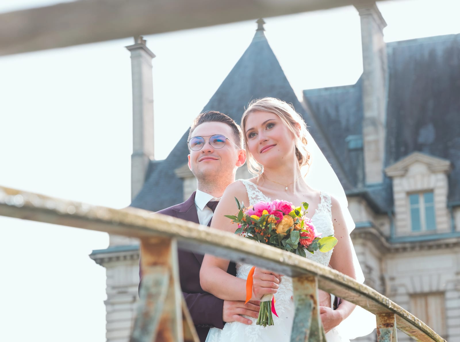 Alex enlace Audrey par derrière sur le pont du domaine, tous deux regardant le ciel, château en fond, mariage au Domaine du Bois Saint Mard, par Jean-Baptiste Argyre (Jaysphotography)