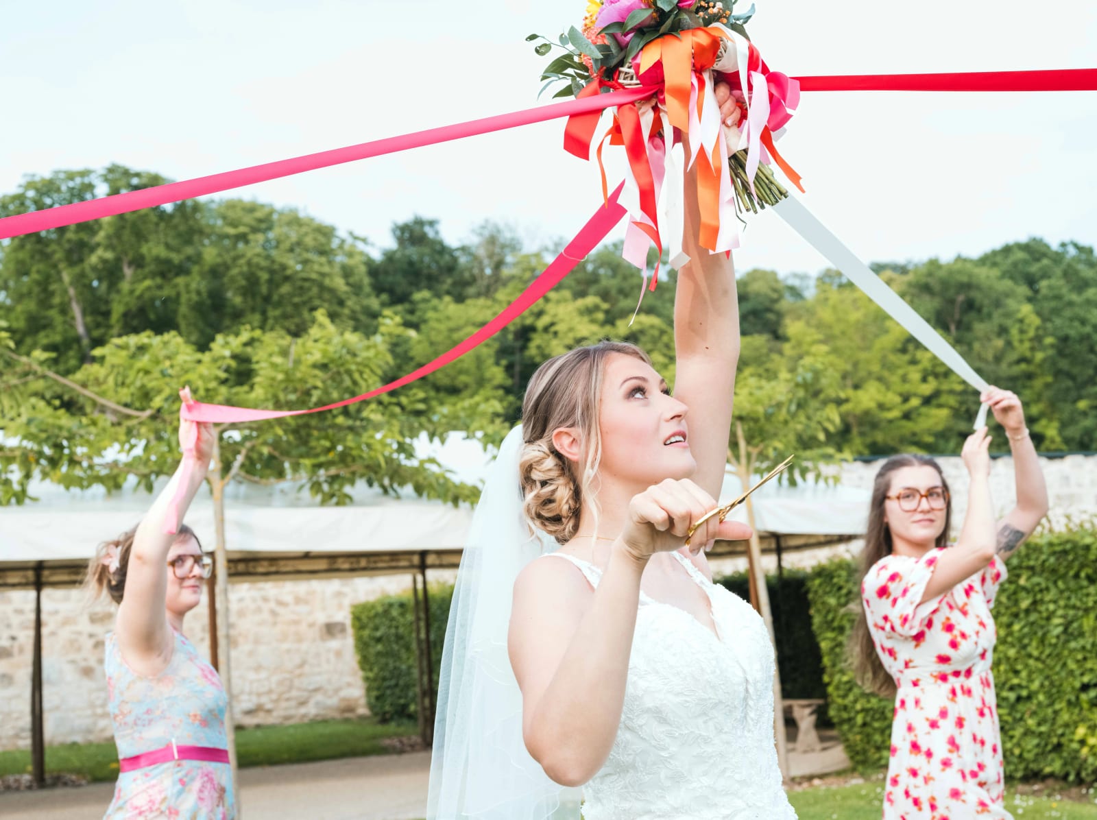 Audrey lève son bouquet et les ciseaux entourée des invitées pendant la ronde des rubans, mariage au Domaine du Bois Saint Mard, par Jean-Baptiste Argyre (Jaysphotography)