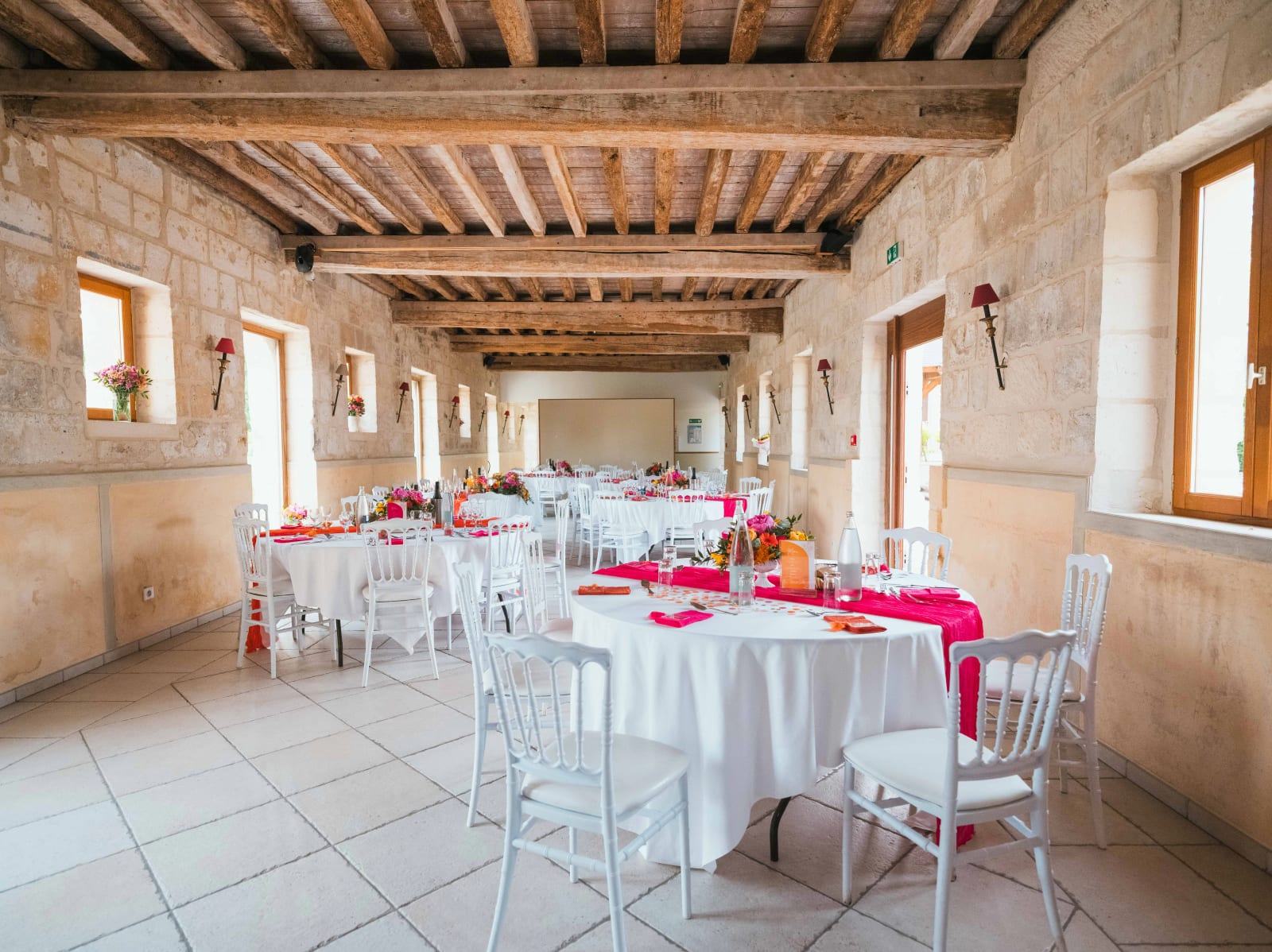 La salle de réception en pierre du Domaine du Bois Saint Mard dressée en blanc et fuchsia avant le repas, mariage au Domaine du Bois Saint Mard, par Jean-Baptiste Argyre (Jaysphotography)