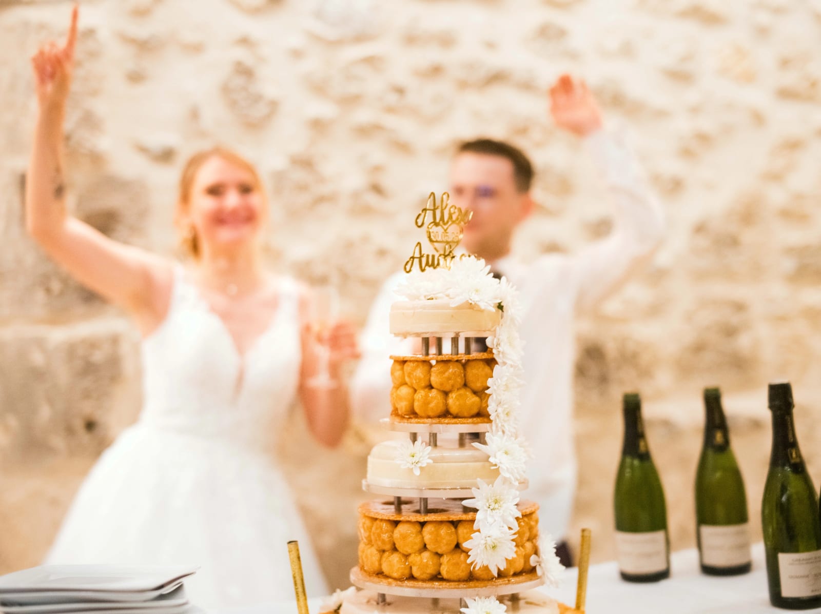 La pièce montée de choux caramel et fleurs blanches avec le topper Alex et Audrey, les mariés derrière, mariage au Domaine du Bois Saint Mard, par Jean-Baptiste Argyre (Jaysphotography)