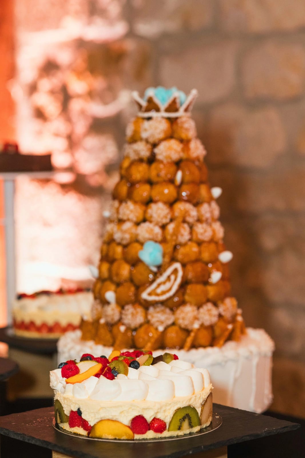 La pièce montée de choux caramélisés couverte de macarons colorés, posée sur un gâteau à étage garni de fruits frais, mariage au Domaine de l'Orangerie, par Jean-Baptiste Argyre (Jaysphotography)