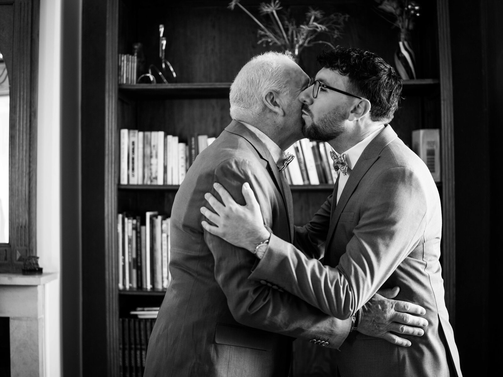 Moment d'émotion en noir et blanc : le marié embrasse un proche devant une bibliothèque — mariage au Domaine du Bois Saint Mard, par Jean-Baptiste Argyre (Jaysphotography)