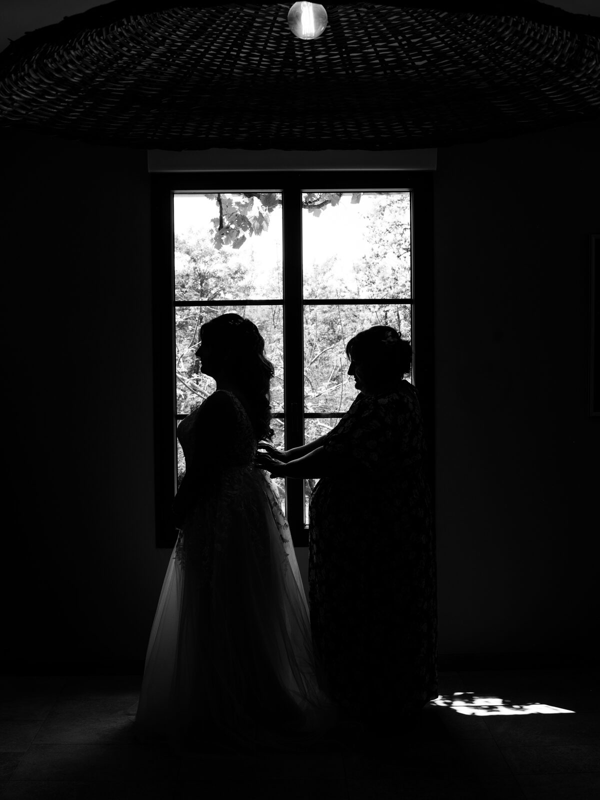 Silhouette en noir et blanc de la mariée et d'un proche devant la grande fenêtre du gîte — mariage au Domaine du Bois Saint Mard, par Jean-Baptiste Argyre (Jaysphotography)