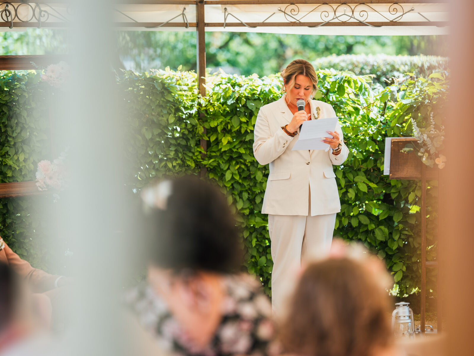 L'officiante en tailleur blanc lit son texte au micro pendant la cérémonie laïque — mariage au Domaine du Bois Saint Mard, par Jean-Baptiste Argyre (Jaysphotography)