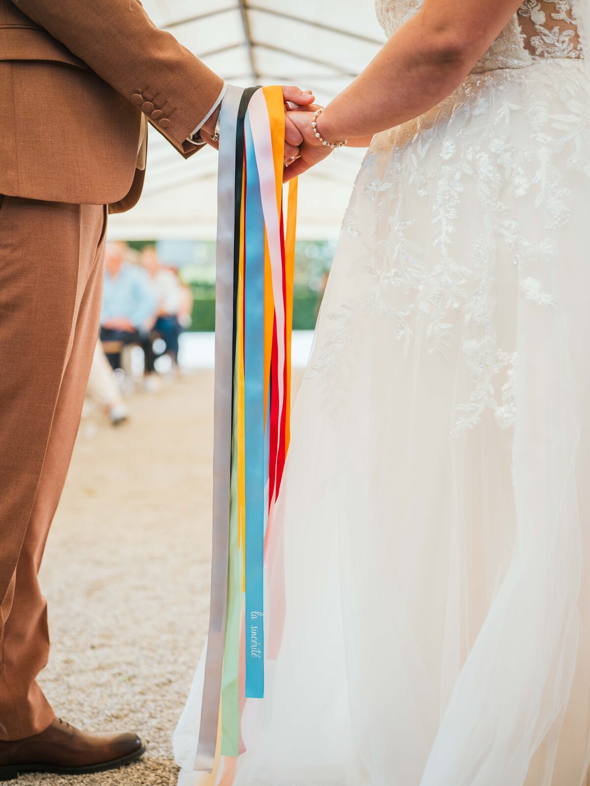 Détail des mains des mariés liées par les rubans colorés lors du rituel de la ronde des rubans — mariage au Domaine du Bois Saint Mard, par Jean-Baptiste Argyre (Jaysphotography)