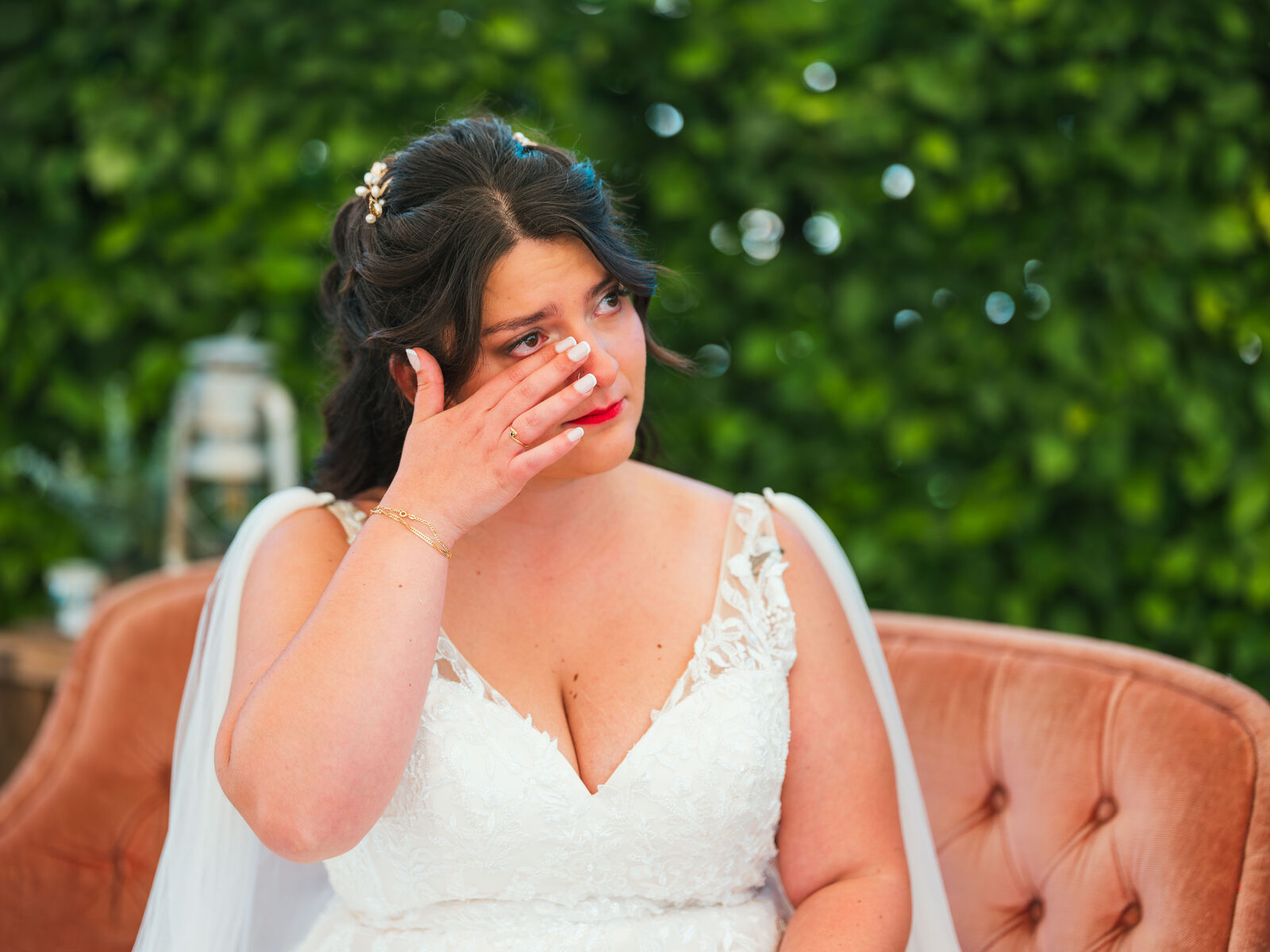 La mariée essuie une larme, assise sur un fauteuil de velours rose pendant la cérémonie — mariage au Domaine du Bois Saint Mard, par Jean-Baptiste Argyre (Jaysphotography)