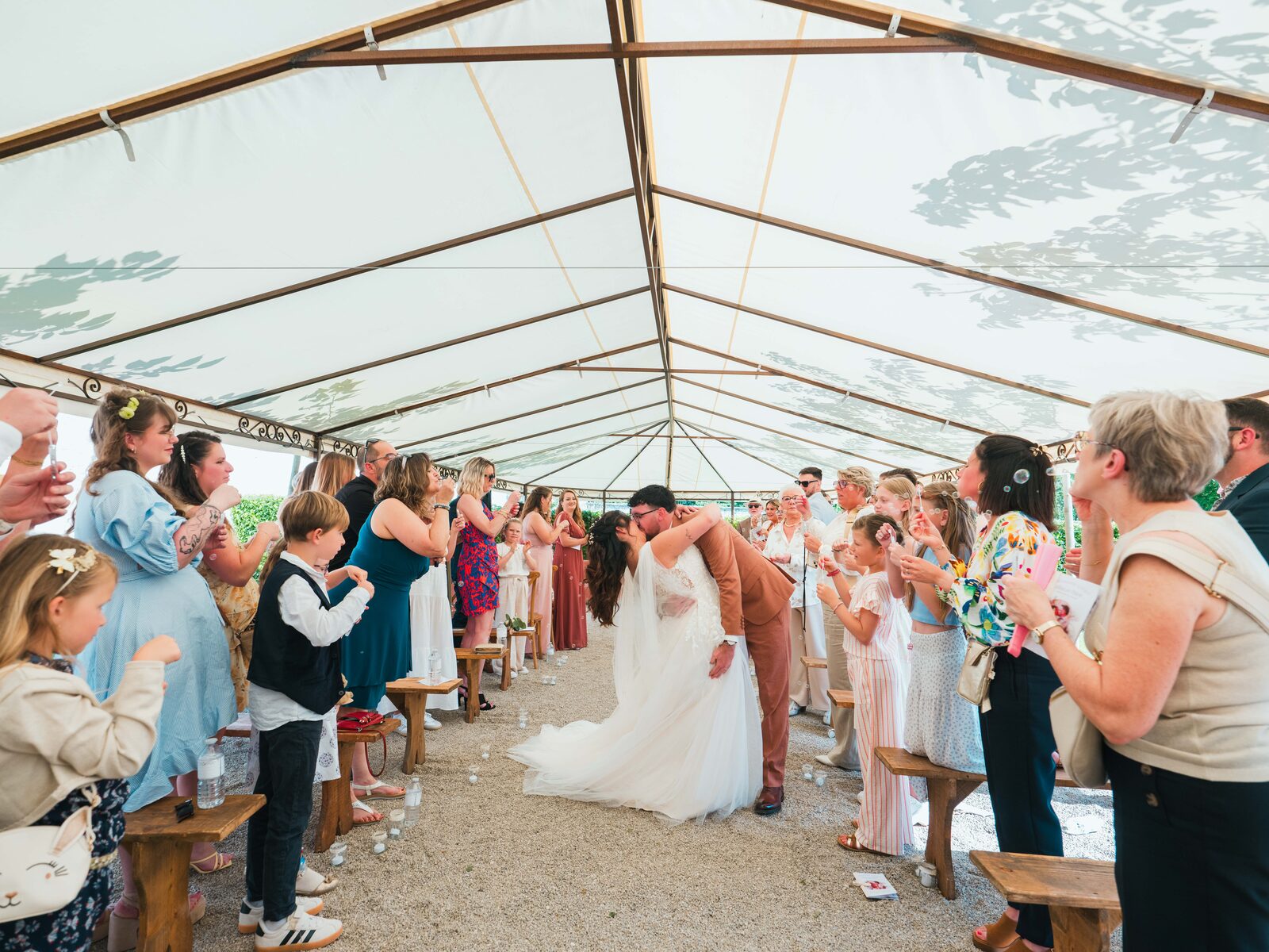 Le baiser des mariés à la sortie de cérémonie, sous la haie d'honneur des invités et des enfants — mariage au Domaine du Bois Saint Mard, par Jean-Baptiste Argyre (Jaysphotography)
