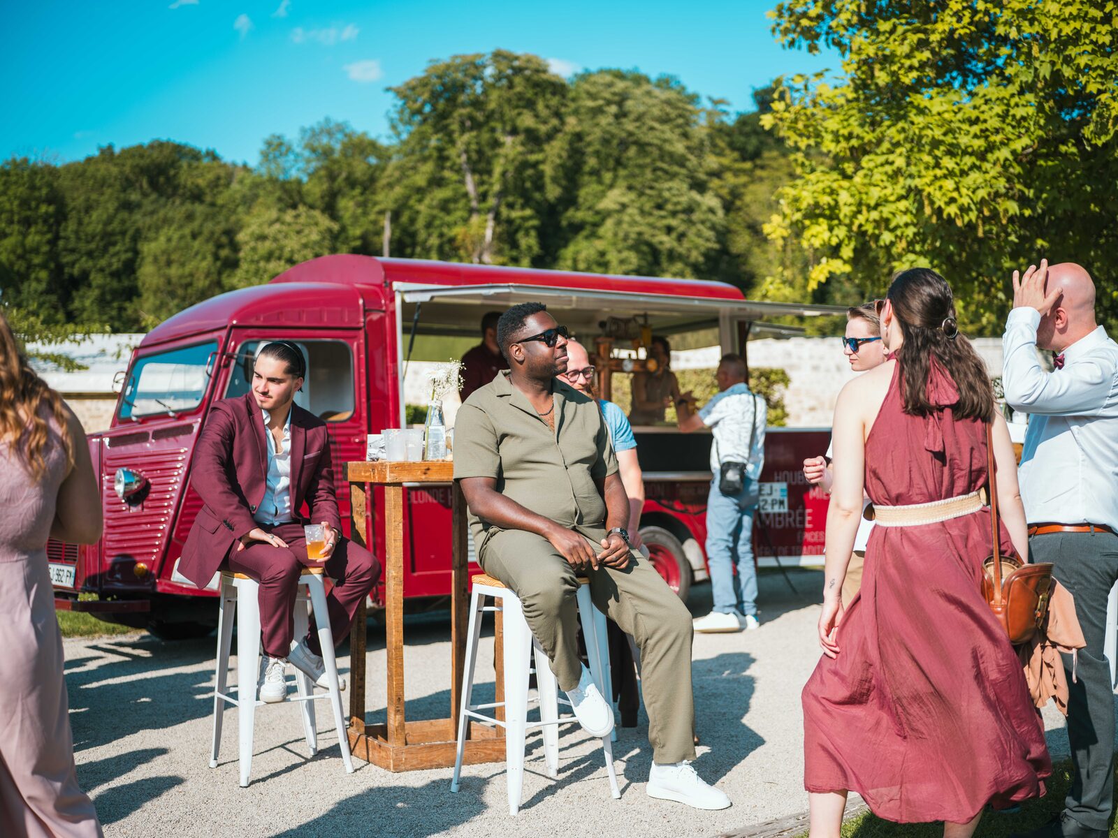 Les invités installés autour du food-truck rouge pendant le vin d'honneur dans le parc ensoleillé — mariage au Domaine du Bois Saint Mard, par Jean-Baptiste Argyre (Jaysphotography)