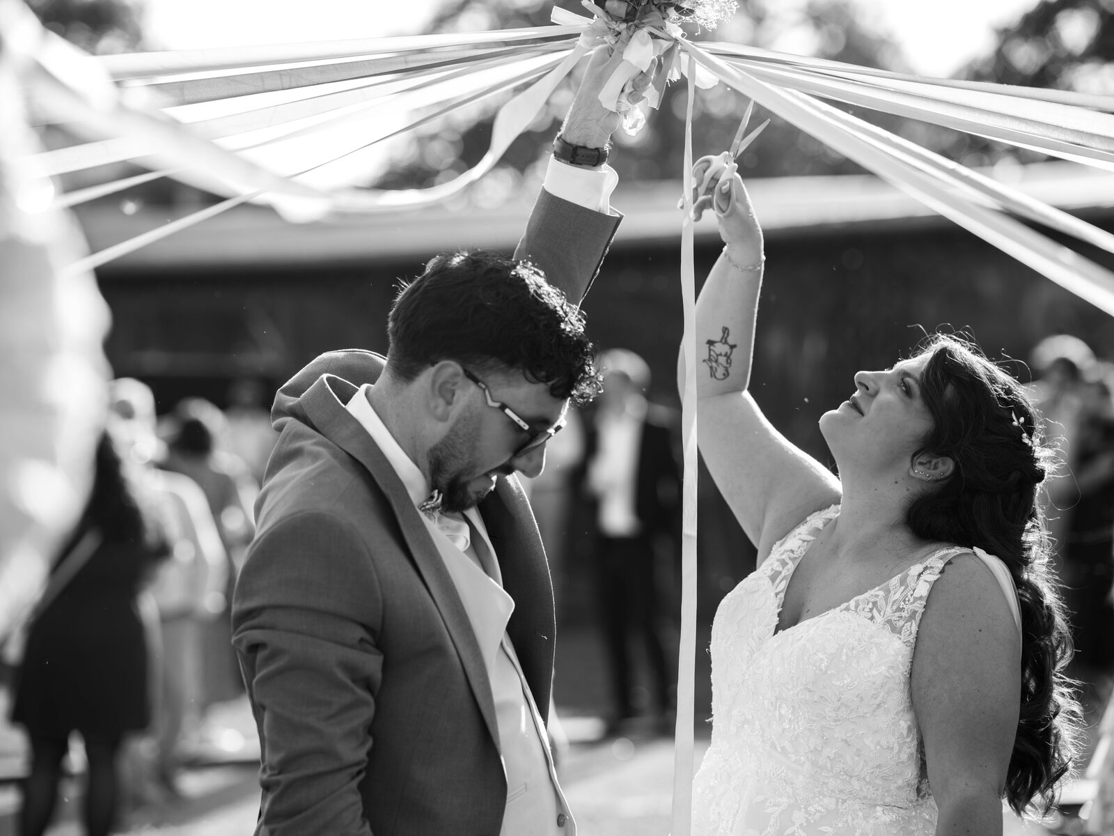 Ronde des rubans en noir et blanc : les mariés lèvent le bouquet tandis que la mariée coupe les rubans — mariage au Domaine du Bois Saint Mard, par Jean-Baptiste Argyre (Jaysphotography)