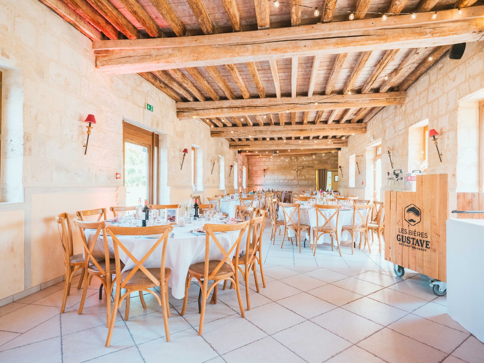 La salle de réception aux poutres apparentes, tables rondes dressées et bar Bières Gustave — mariage au Domaine du Bois Saint Mard, par Jean-Baptiste Argyre (Jaysphotography)