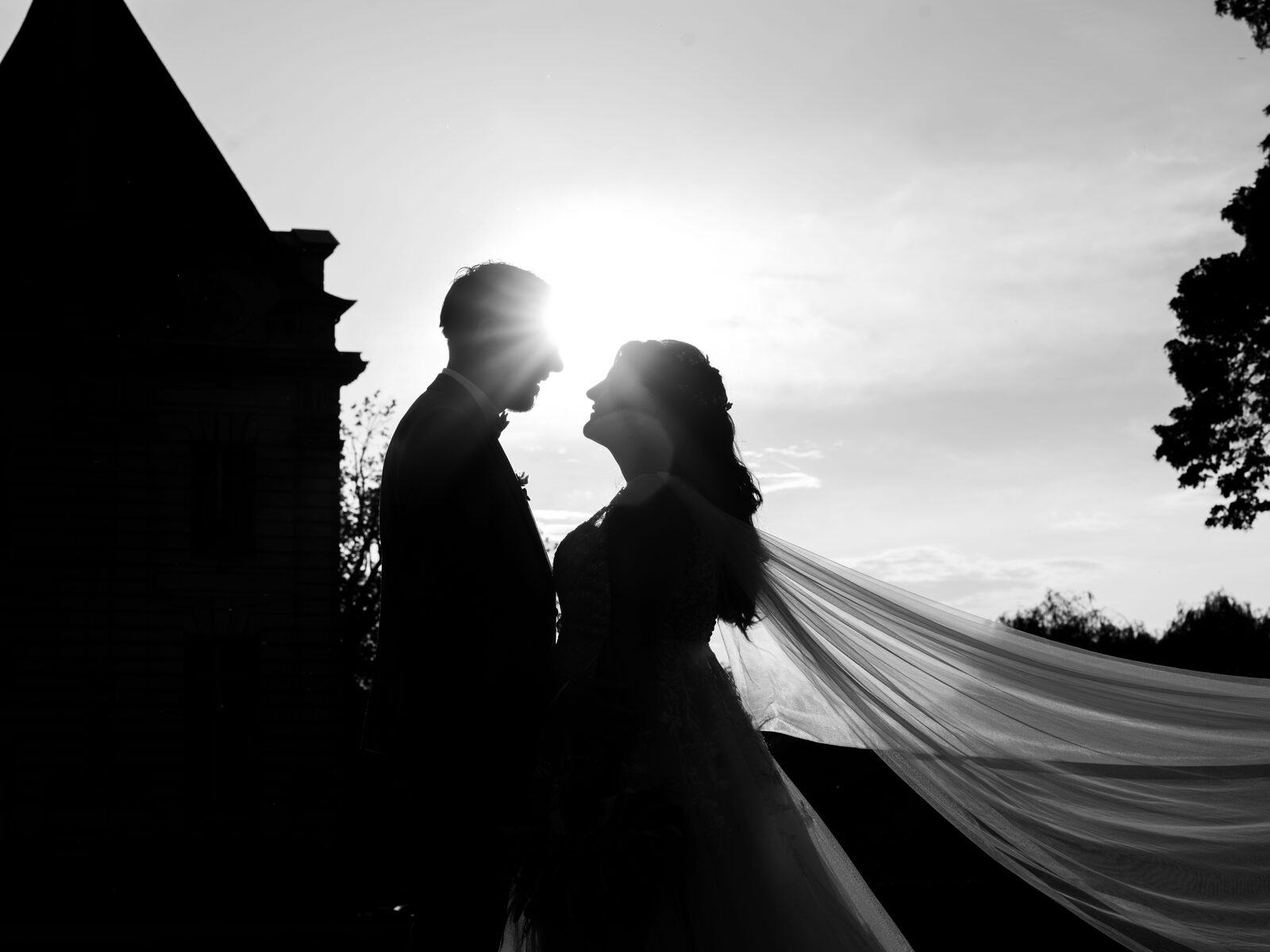 Silhouette des mariés en contre-jour, le voile envolé par le vent, face au soleil couchant — mariage au Domaine du Bois Saint Mard, par Jean-Baptiste Argyre (Jaysphotography)