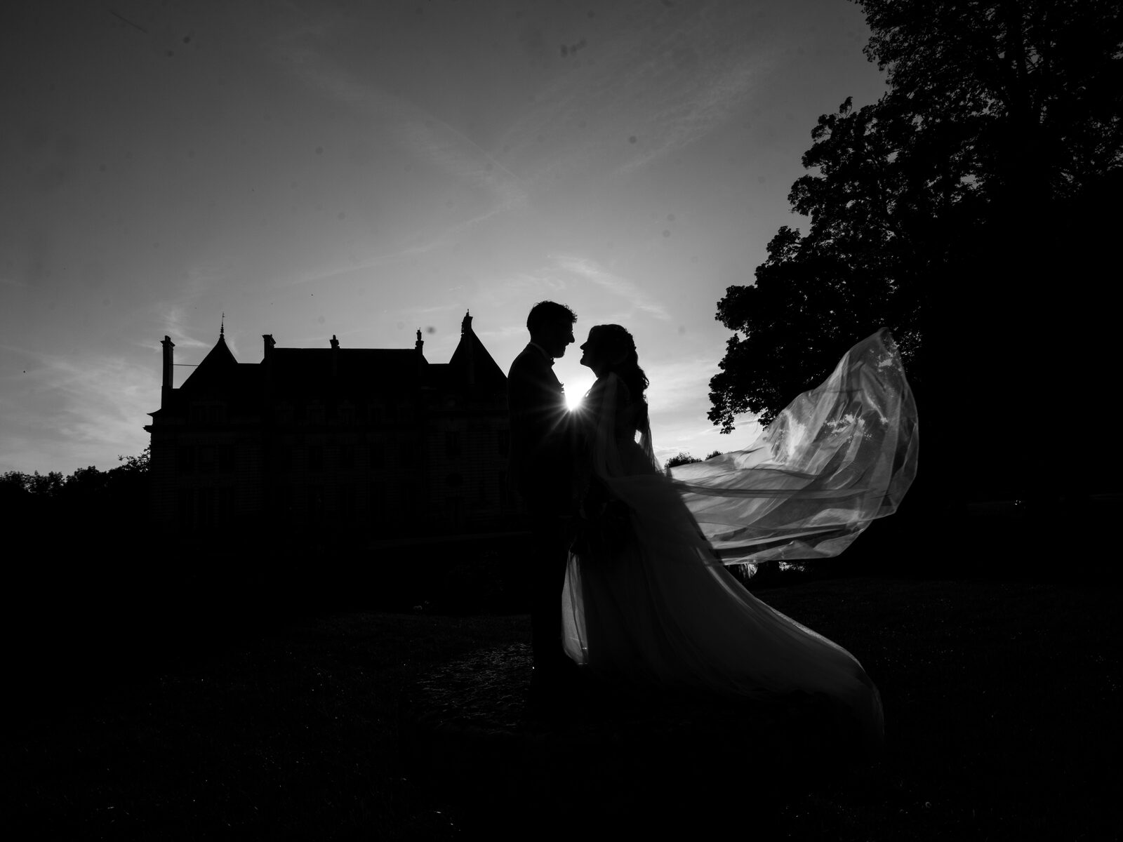 Silhouette noir et blanc des mariés et du voile au vent, le château se découpant dans le ciel — mariage au Domaine du Bois Saint Mard, par Jean-Baptiste Argyre (Jaysphotography)