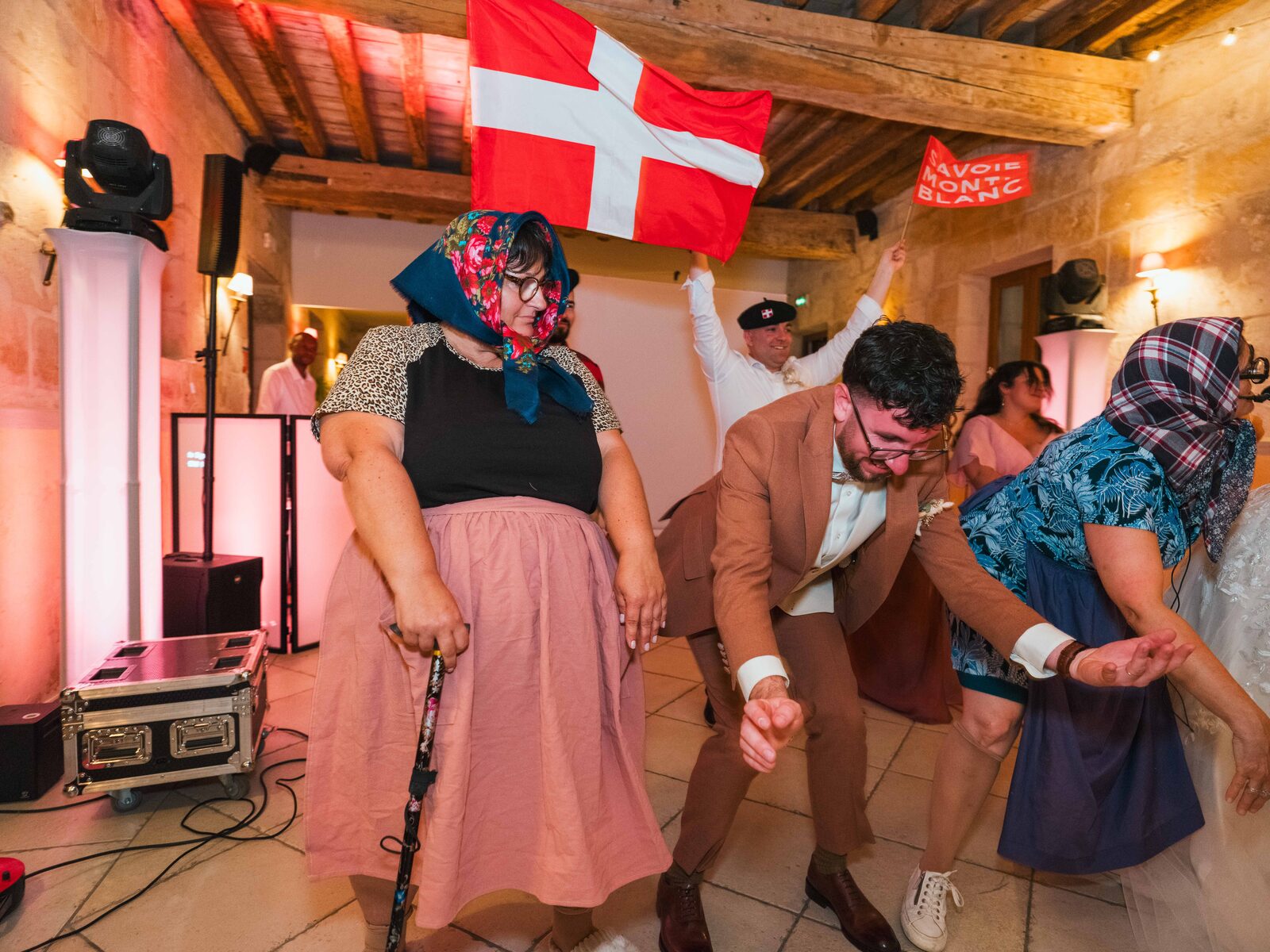 Animation dansante : une invitée coiffée d'un foulard et un drapeau Savoie Mont-Blanc derrière le marié — mariage au Domaine du Bois Saint Mard, par Jean-Baptiste Argyre (Jaysphotography)