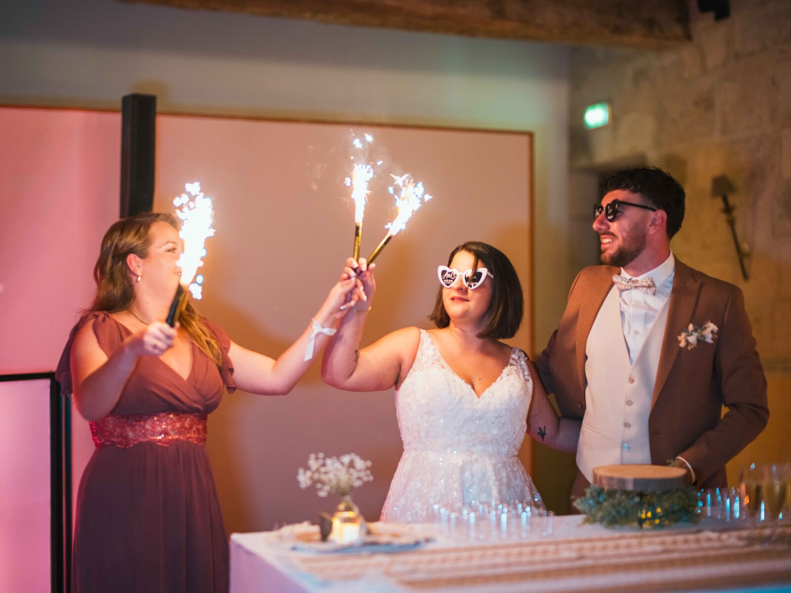 Les mariés et un témoin lèvent des cierges magiques au-dessus du dessert, lunettes en cœur — mariage au Domaine du Bois Saint Mard, par Jean-Baptiste Argyre (Jaysphotography)