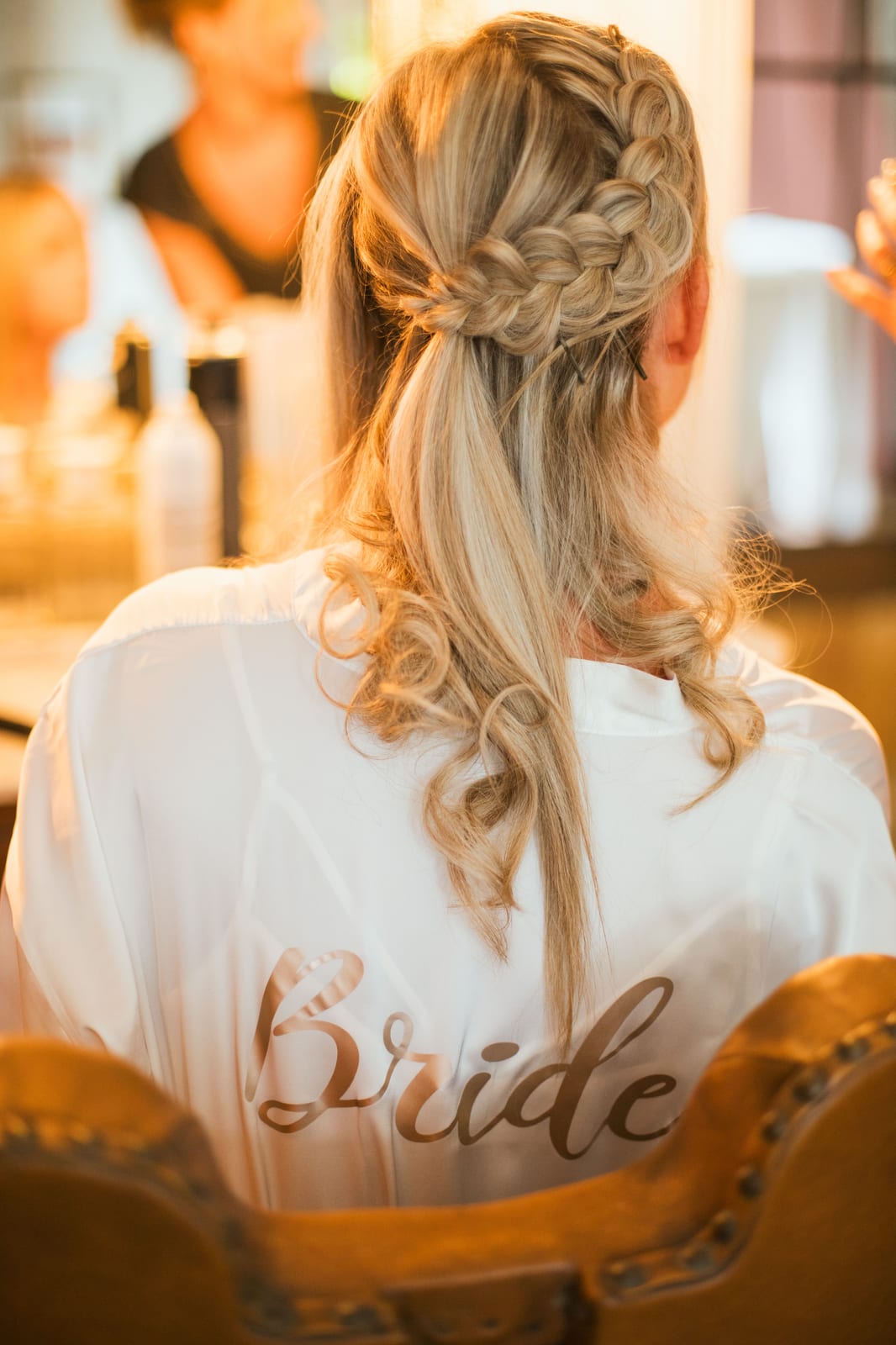 Amandine de dos en peignoir de mariée "Bride", coiffure tressée blonde et boucles, pendant la mise en beauté, mariage au Domaine de Senercy, par Jean-Baptiste Argyre (Jaysphotography)